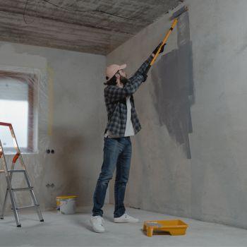 Man Painting Grey Concrete Wall Inside with Roller Brush